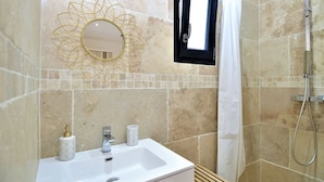 Ein Badezimmer mit einem weißen Waschbecken, einem goldfarbenen Spiegel und einer Dusche.