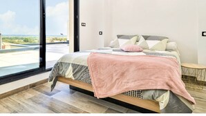 Ein Schlafzimmer mit großem Fenster, einem Bett mit gemusterten Textilien und einem kleinen runden Tisch.