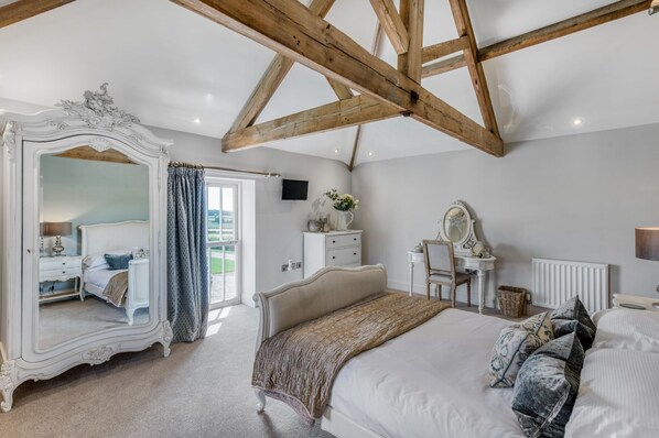 A bedroom with a large bed, a dresser, a vanity with a mirror, and a wardrobe with a mirror.