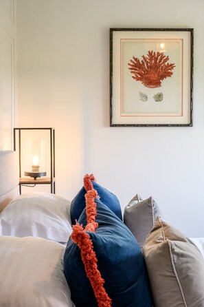 A bed with pillows and a decorative tassel, a framed artwork on the wall, and a bedside table with a lamp.