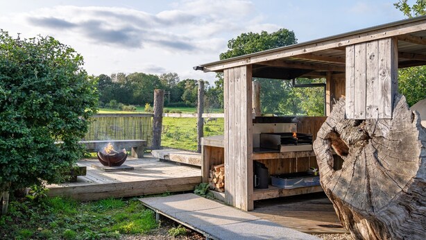 A rustic outdoor kitchen area with a fire pit, wooden structure, and a large tree stump.