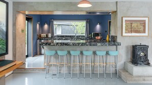 A modern kitchen with a bar area, featuring a stone countertop, bar stools, and a pendant light.
