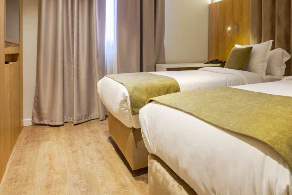 A hotel room with two beds, a wooden wardrobe, and a curtain.