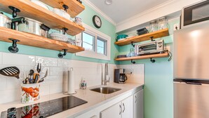 A kitchen with white cabinets, wooden shelves, a stainless steel refrigerator, and a window above the sink.