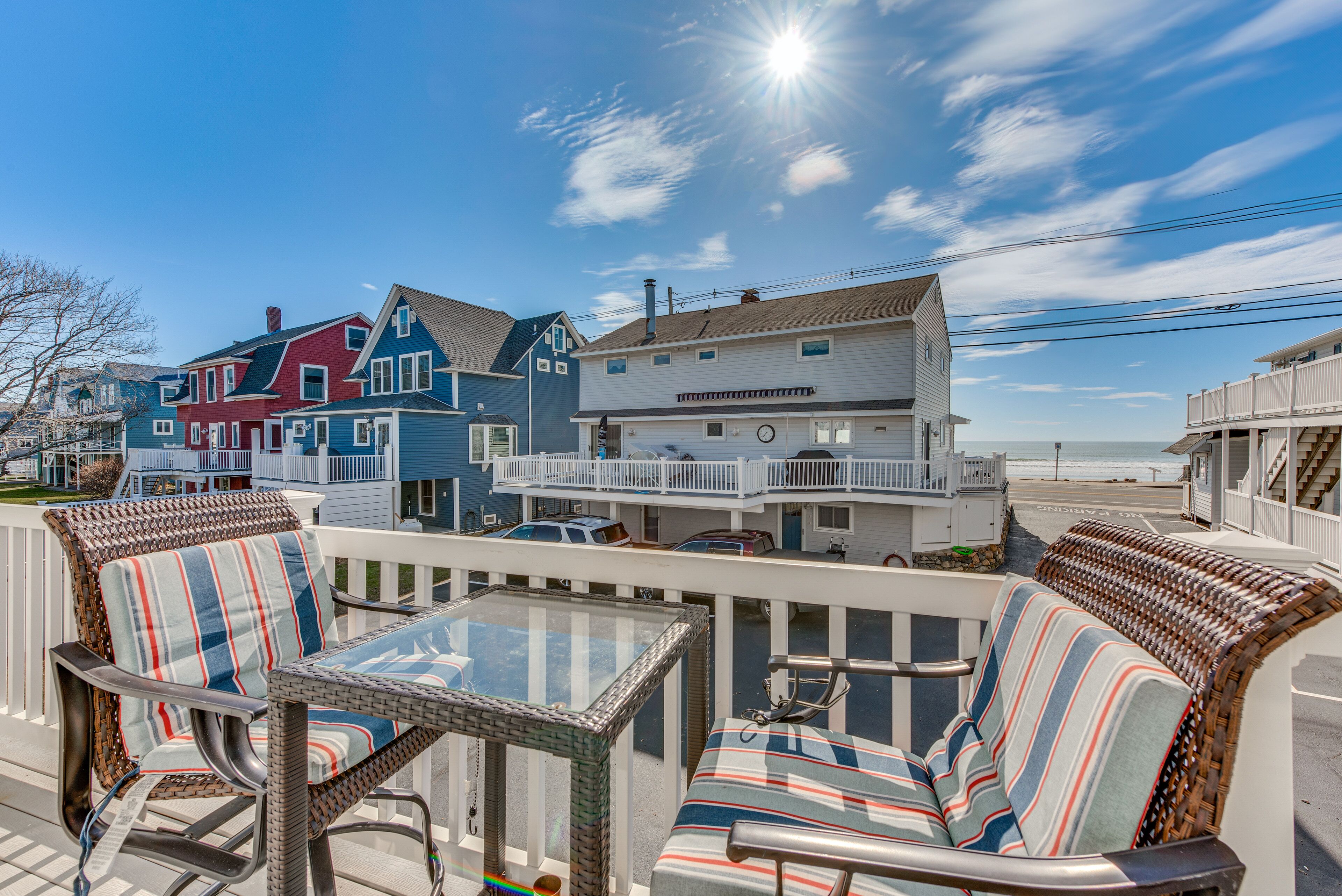 A coastal view with a balcony seating area featuring wicker chairs and a glass table.
