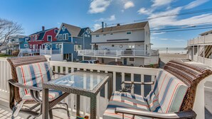 A coastal view with a balcony seating area featuring wicker chairs and a glass table.