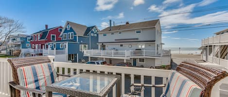 A coastal view with a balcony seating area featuring wicker chairs and a glass table.
