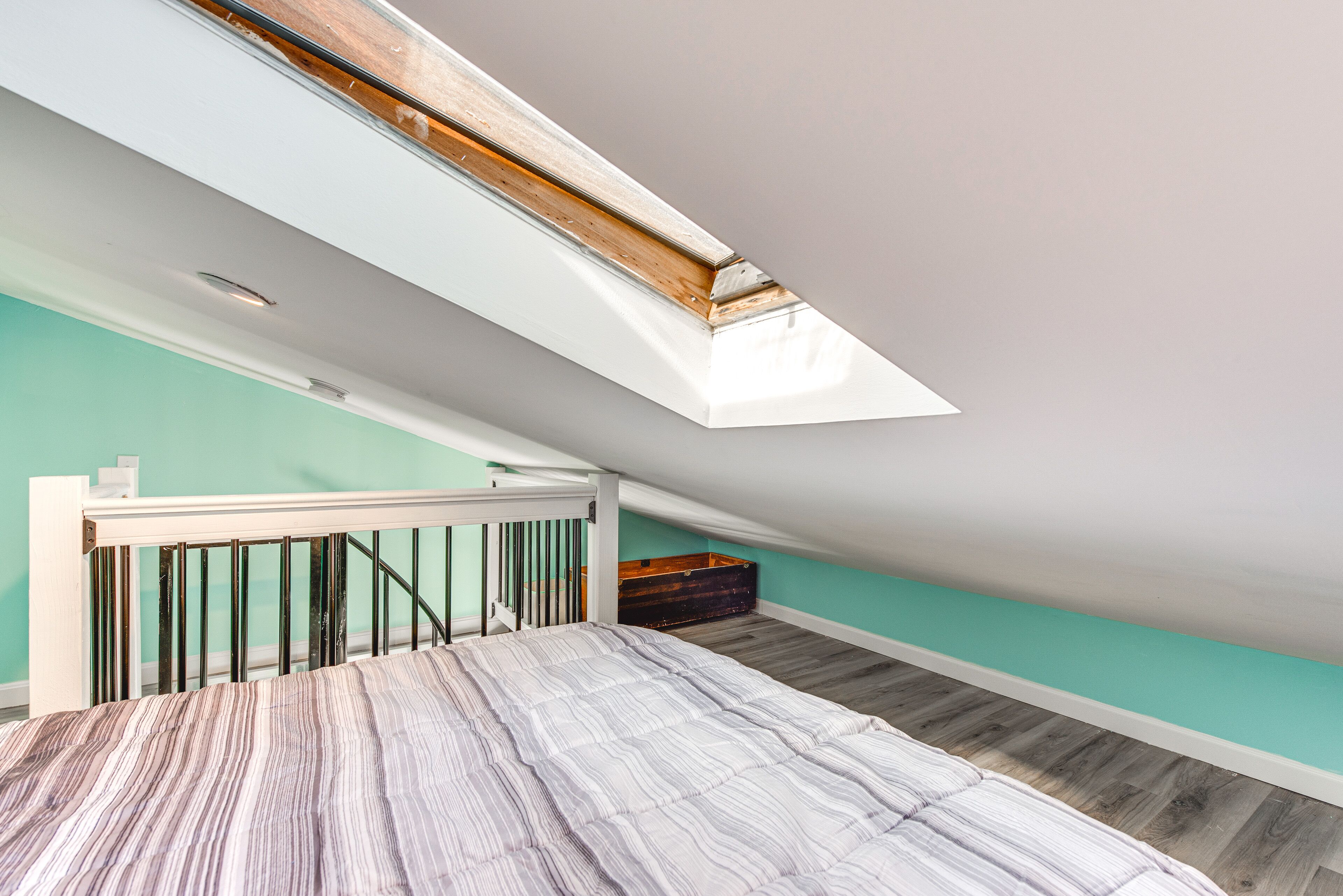 Een slaapkamer met een schuine kap, een dakraam, een bed met een gestreept dekbed en een houten dressoir.