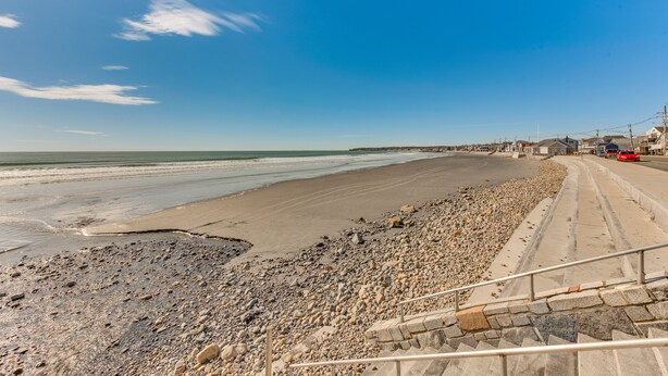 A beach with a pebble path leading to the water, a staircase, and a red bus in the distance.