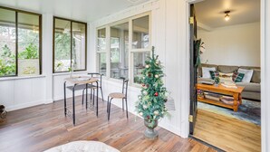 Ein Zimmer mit Holzboden, einem Esstisch mit Stühlen, einem Weihnachtsbaum und einer Couch mit Kissen.