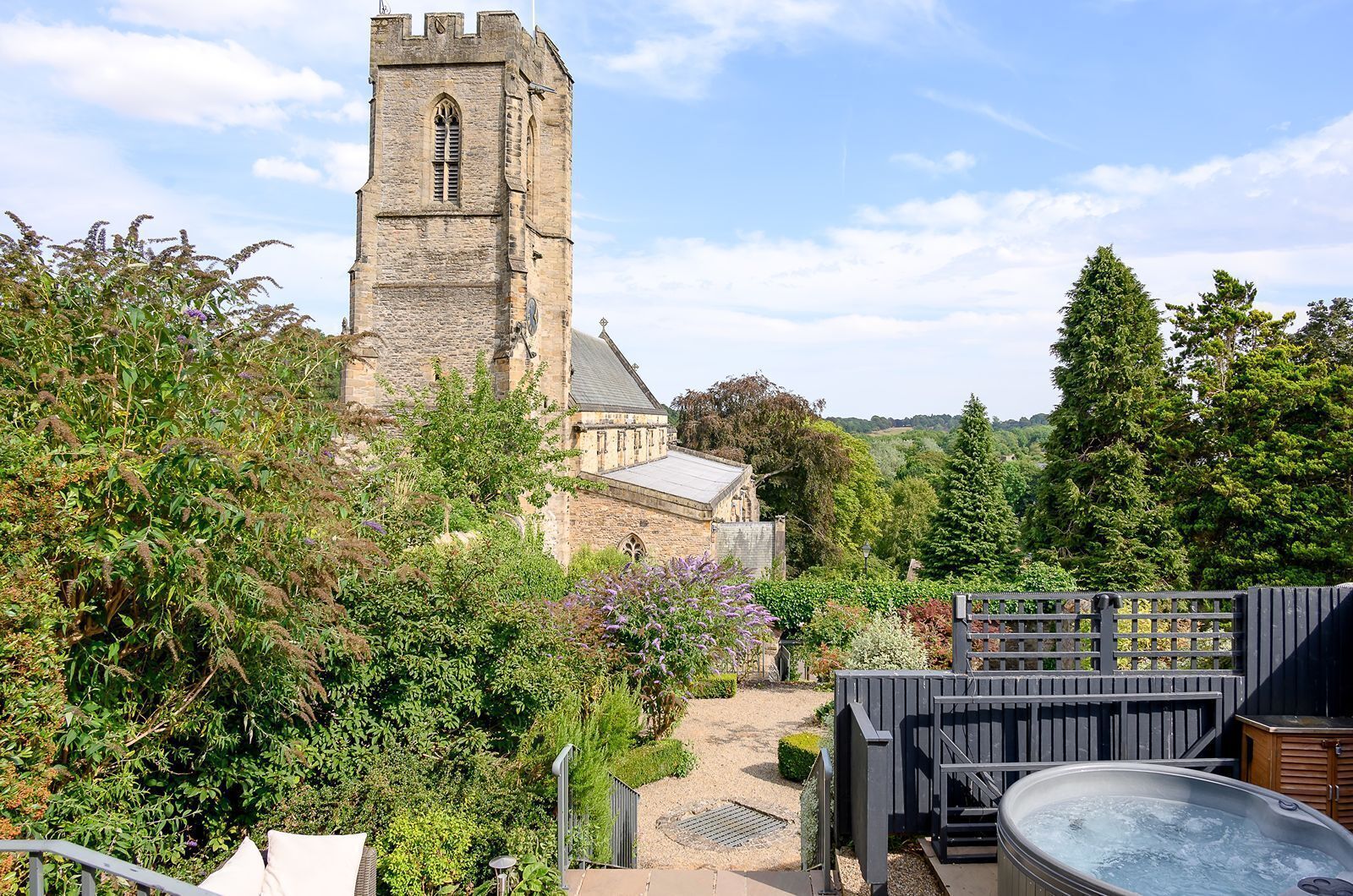 A historic stone tower with a clock, surrounded by lush greenery and a hot tub area.