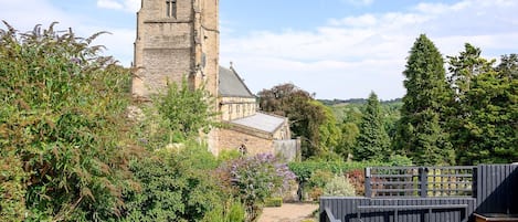 A historic stone tower with a clock, surrounded by lush greenery and a hot tub area.