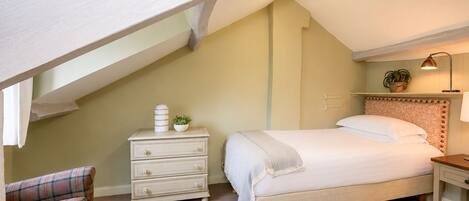 A bedroom with a sloped ceiling, a bed with a headboard, a bedside table with a lamp, a dresser, and a chair.