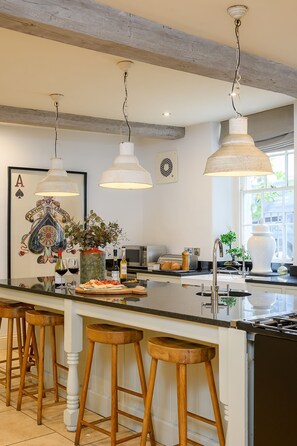A kitchen with a central island, wooden stools, pendant lighting, and a framed playing cards artwork. - 30 Frenchgate -  a house that sleeps 10 guests  in 5 bedrooms (Richmond)