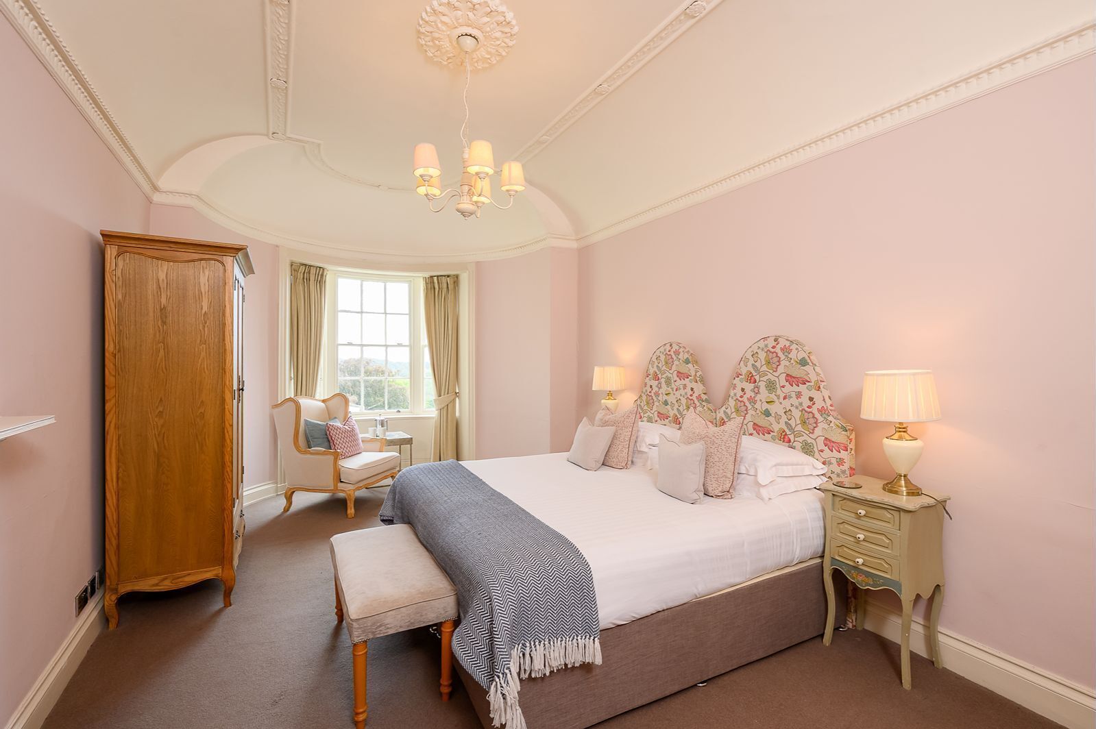 Bedroom at 30 Frenchgate with Zip and Lock double bed, floral upholstered headboards, bedside tables and lamps, and a bay window seating area with armchair and countryside views.