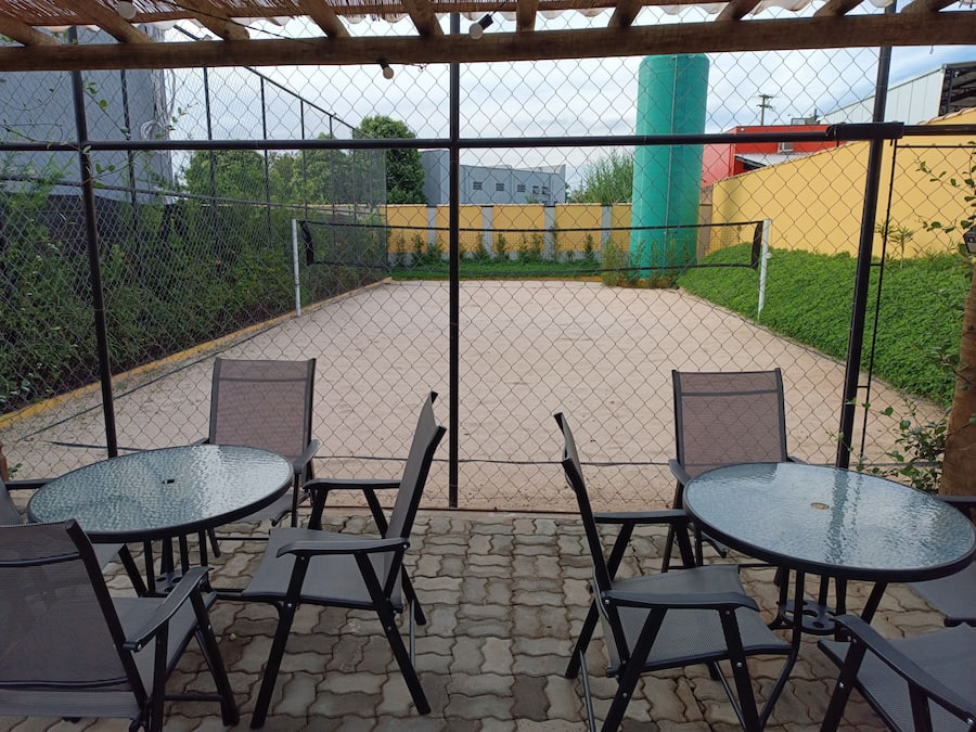 Un patio al aire libre con cerca de malla, asientos cubiertos y superficie pavimentada.