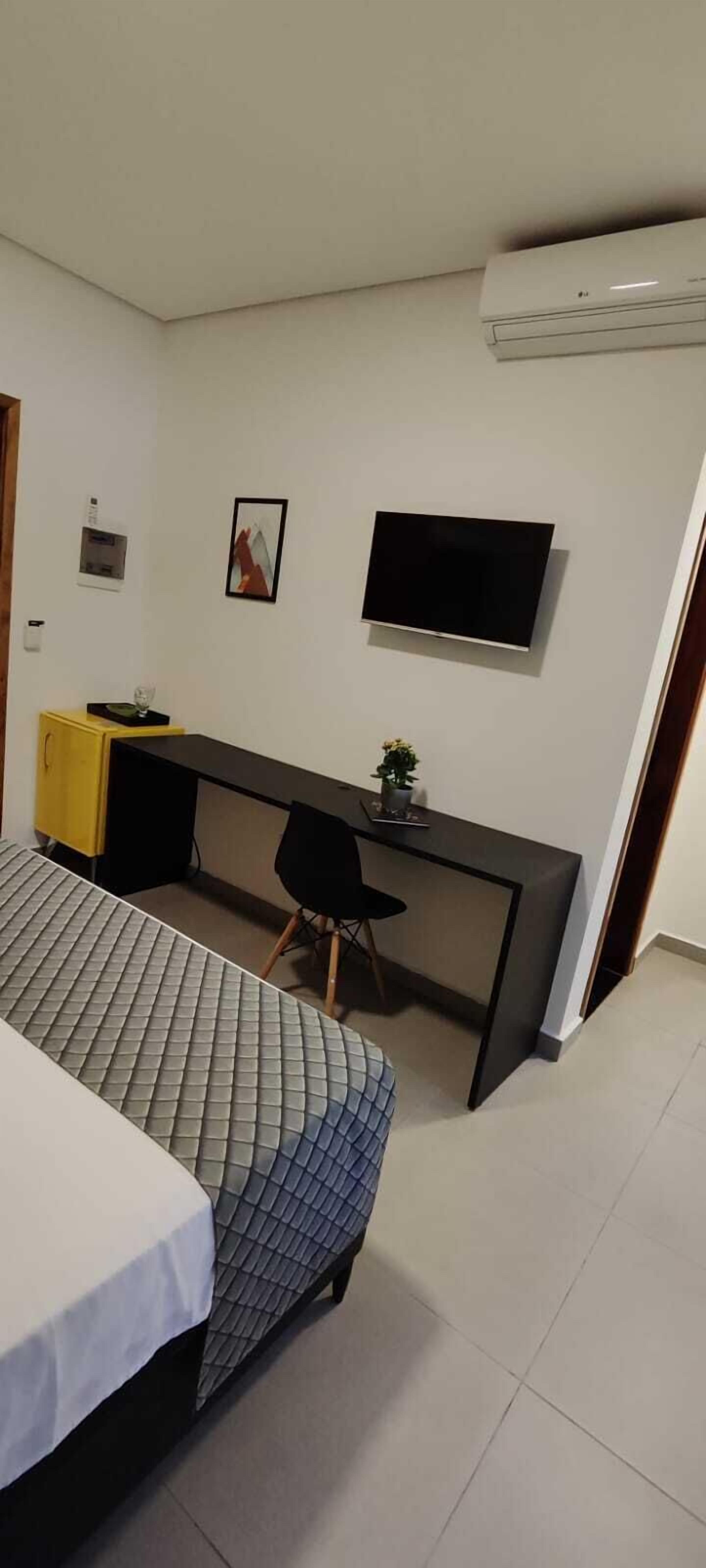 Un dormitorio con cama, escritorio, silla, televisor y aire acondicionado.