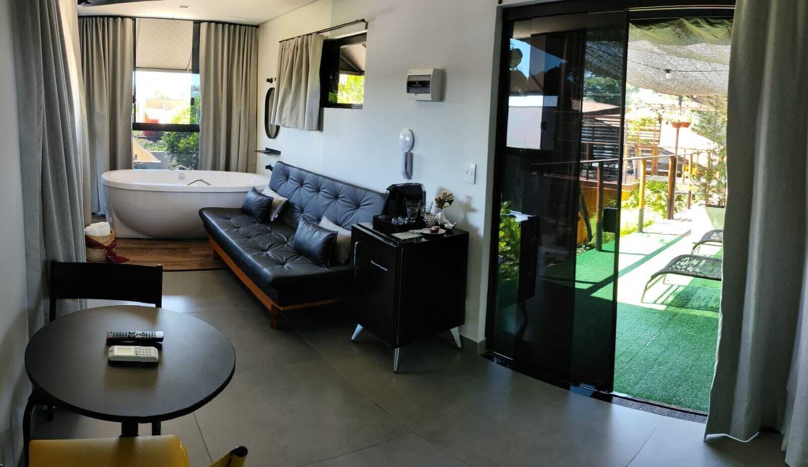A modern living room with a sofa, a small table, a glass-enclosed balcony with outdoor furniture.