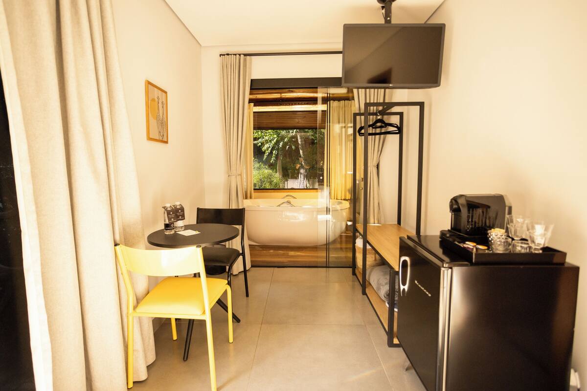 Una habitación de hotel compacta con zona de comedor, bañera, televisor de pantalla plana y refrigerador.
