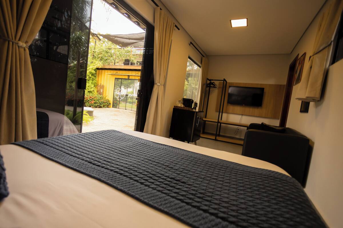 Habitación de hotel con cama, televisor montado en la pared y puerta corrediza que da a un área exterior.