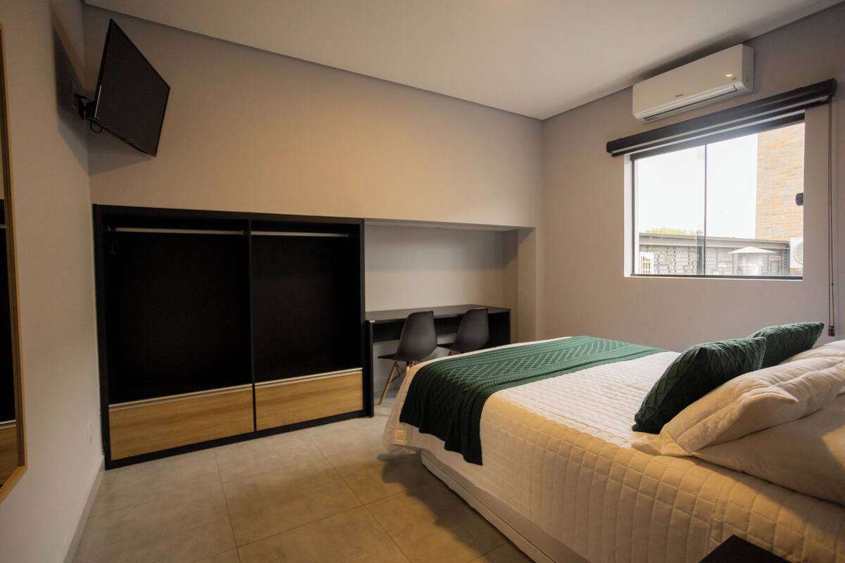 Un dormitorio con cama, escritorio, silla, armario y ventana con vistas.
