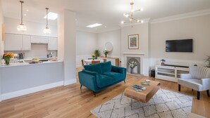 A modern living room with a teal sofa, a coffee table, and a fireplace. There is a kitchen area with white cabinets and a dining table. - The Swaledale -  a cottage that sleeps 2 guests  in 1 bedroom (Richmond)