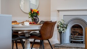 Un comedor con una mesa blanca, sillas de cuero marrón, una cafetera y un florero con flores.