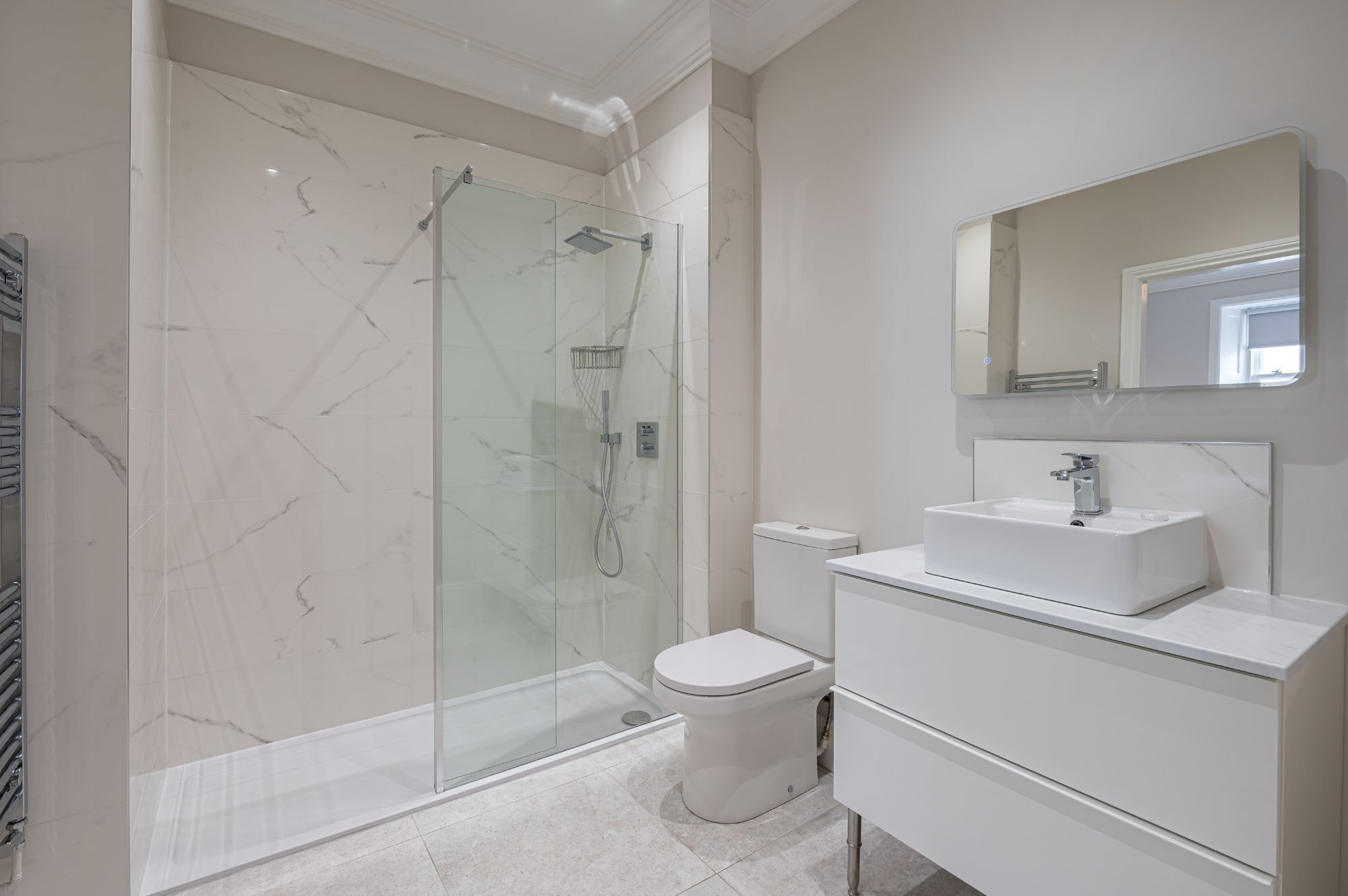 Un baño moderno con ducha de vidrio, inodoro blanco y lavamanos blanco con espejo arriba.