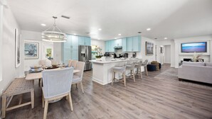 A modern kitchen with light blue cabinets, a central island, and a dining area with wicker chairs. - Tropical Oasis with Private Pool & Spa, minutes from Siesta Key Beach! (Sarasota)