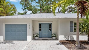 A single-story house with a light blue garage door, a matching front door, and a small porch area with two potted plants. - Tropical Oasis with Private Pool & Spa, minutes from Siesta Key Beach! (Sarasota)