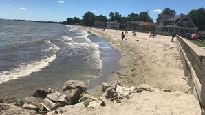 A beach with waves, a sandy shore, and houses in the background. - Actual Pretty Boy Floyd Hideout  Lake Erie, MI (Luna Pier)