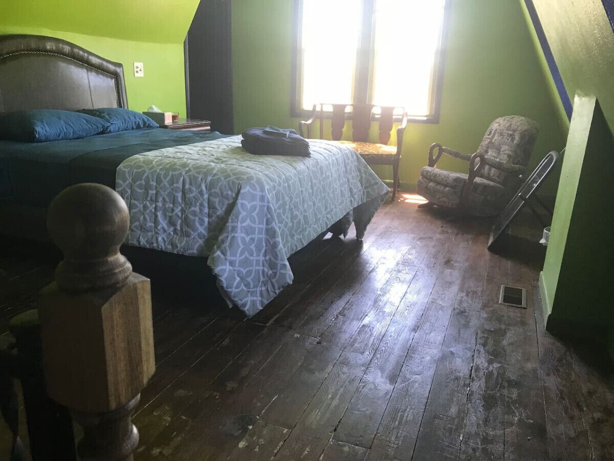 A bedroom with a bed, a chair, and a wooden floor.