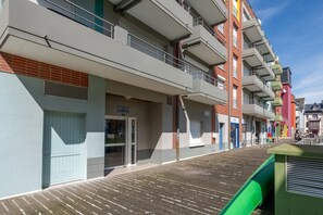 Ein mehrstöckiges Hotel mit Balkonen, einer Holzterrasse und einem grünen Markisenvorbau.