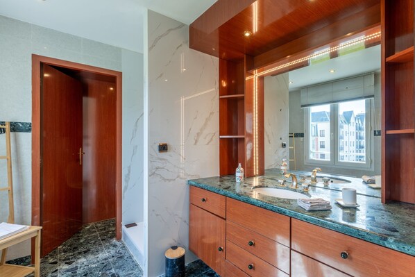 Een moderne badkamer met een houten wastafelmeubel, marmeren wanden en een grote spiegel.