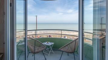 Un balcon avec vue sur la plage, des fauteuils en osier et une petite table.