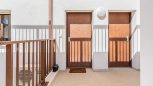 Un couloir avec deux portes, une rambarde en bois et un sol carrelé.