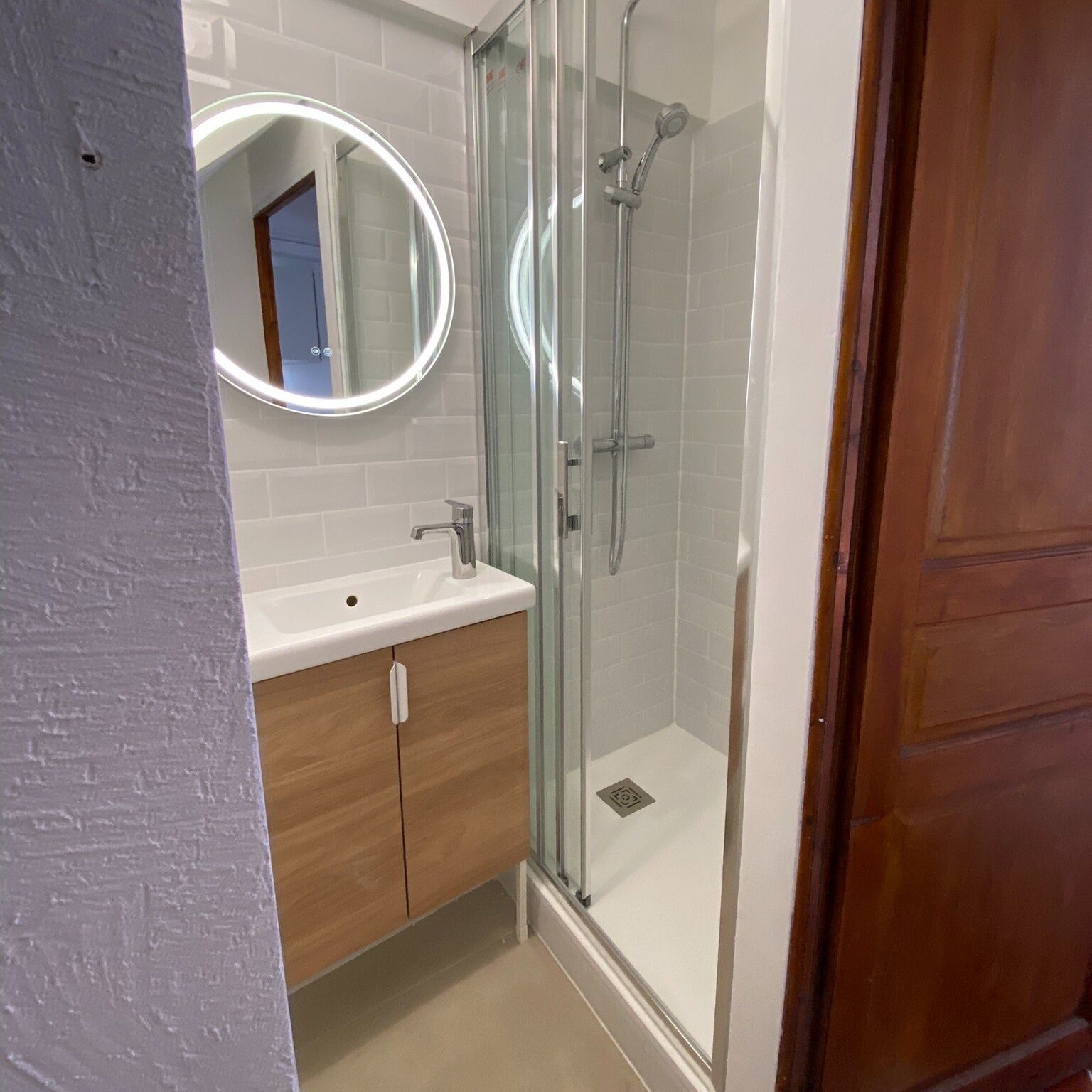 Un baño moderno con ducha de vidrio, lavamanos blanco y armario de madera.