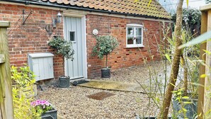 A brick house with a tiled roof, a white door, and a window. There are potted plants and a gravel driveway. - 2 bedroom accommodation in Overstrand, near Cromer (Overstrand, near Cromer)