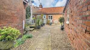 A narrow brick alleyway with a stone pathway, a white door, and a small garden area with potted plants. - 2 bedroom accommodation in Overstrand, near Cromer (Overstrand, near Cromer)