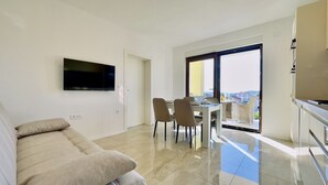 Ein modernes Wohnzimmer mit einer Couch, einem Esstisch mit Stühlen, einem flachbildfernseher an der Wand und einem Balkon mit Blick.