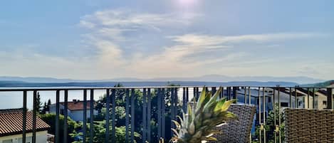 A balcony with a table set with fruits and a striped bowl, overlooking a scenic view of mountains and a body of water.