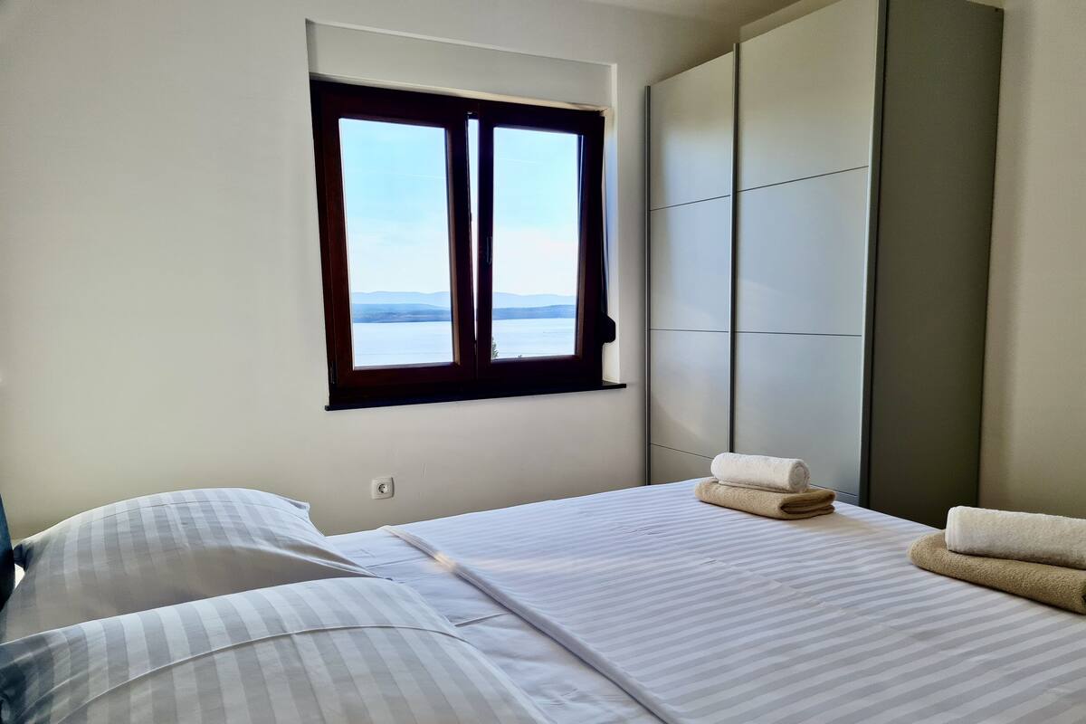 A bedroom with a bed, pillows, a window with a view, and a wardrobe.