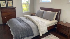 Ein Schlafzimmer mit einem Bett, Nachttischen, einer Kommode und zwei Fenstern.