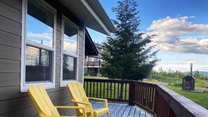 Eine Holzterrasse mit zwei gelben Adirondack-Stühlen, einem Hollerdgrund und Blick auf eine grüne Landschaft.