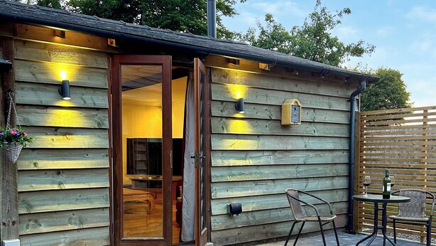 A wooden cabin with a sliding glass door, a small patio with a table and chairs, and outdoor lighting.