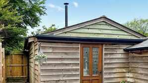 A wooden cabin with a green roof, a wooden door with glass panels, and two potted plants on either side of the door.