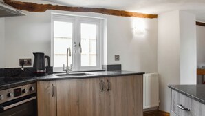 A kitchen with wooden cabinets, a black countertop, a double sink, a kettle, and an oven.