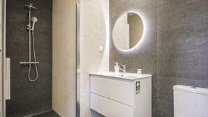A modern bathroom with a shower, a sink with a mirror, and a toilet. - Casa da Oliveira III by Homie (Santa Cruz)