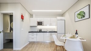 A modern kitchen with white cabinets, a black countertop, and a dining area with a white table and chairs. - Casa da Oliveira III by Homie (Santa Cruz)