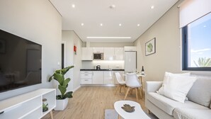 A modern living room with a flat-screen TV, a sofa, a coffee table, and a dining area with a table and chairs. - Casa da Oliveira III by Homie (Santa Cruz)